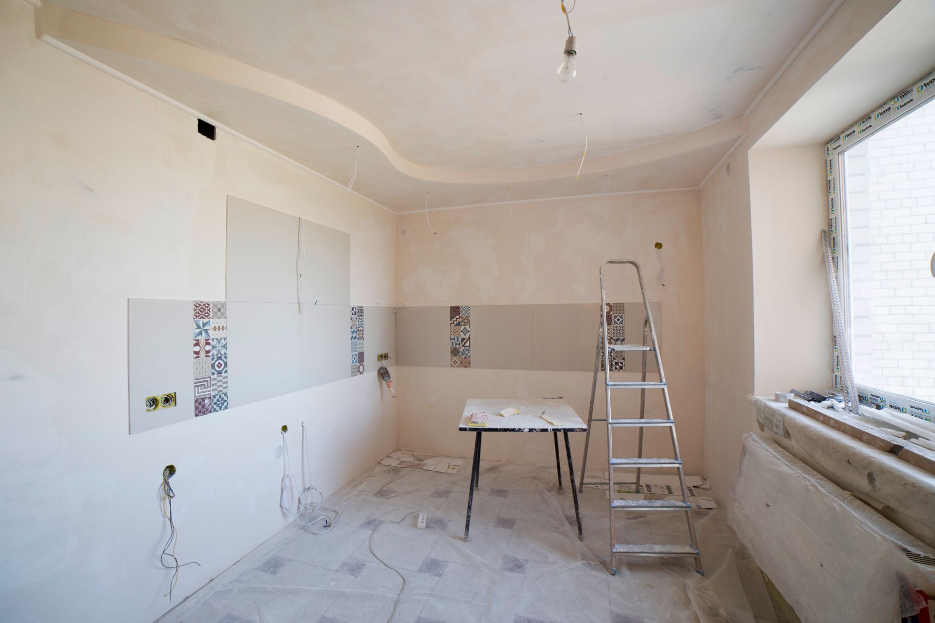 Stanza in ristrutturazione a Bologna con scala, tavolo, piastrelle decorative e cavi elettrici sul pavimento.